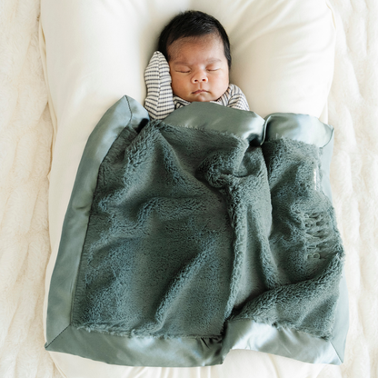 Baby boy snuggled in Evergreen Satin Border mini baby blanket. 