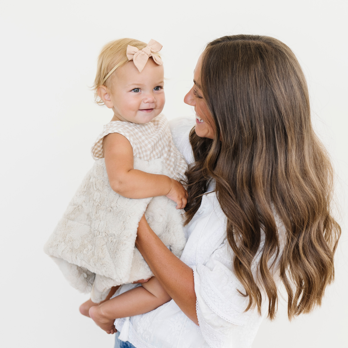 Mom holding baby girl snugged with an oat tan dream faux fur mini baby blanket. 