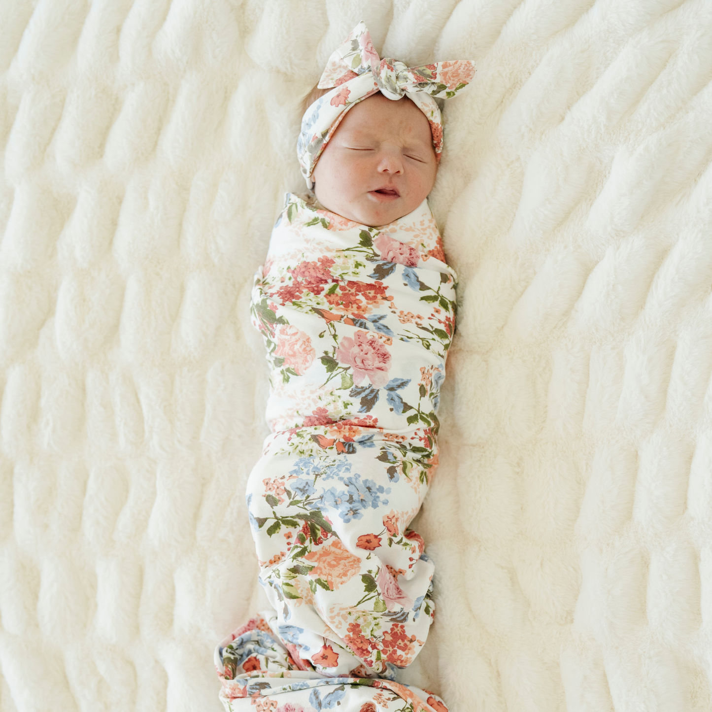 Baby girl swaddled in Vintage Floral Saranoni stretchy soft swaddle with a matching bow.