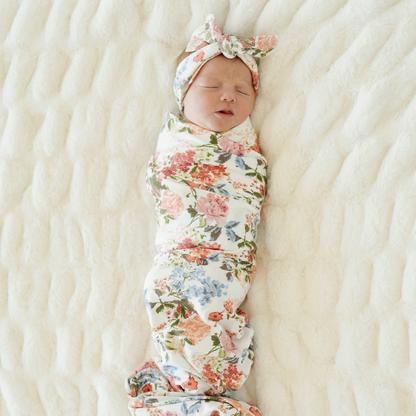 Baby girl swaddled in Vintage Floral Saranoni stretchy soft swaddle with a matching bow.