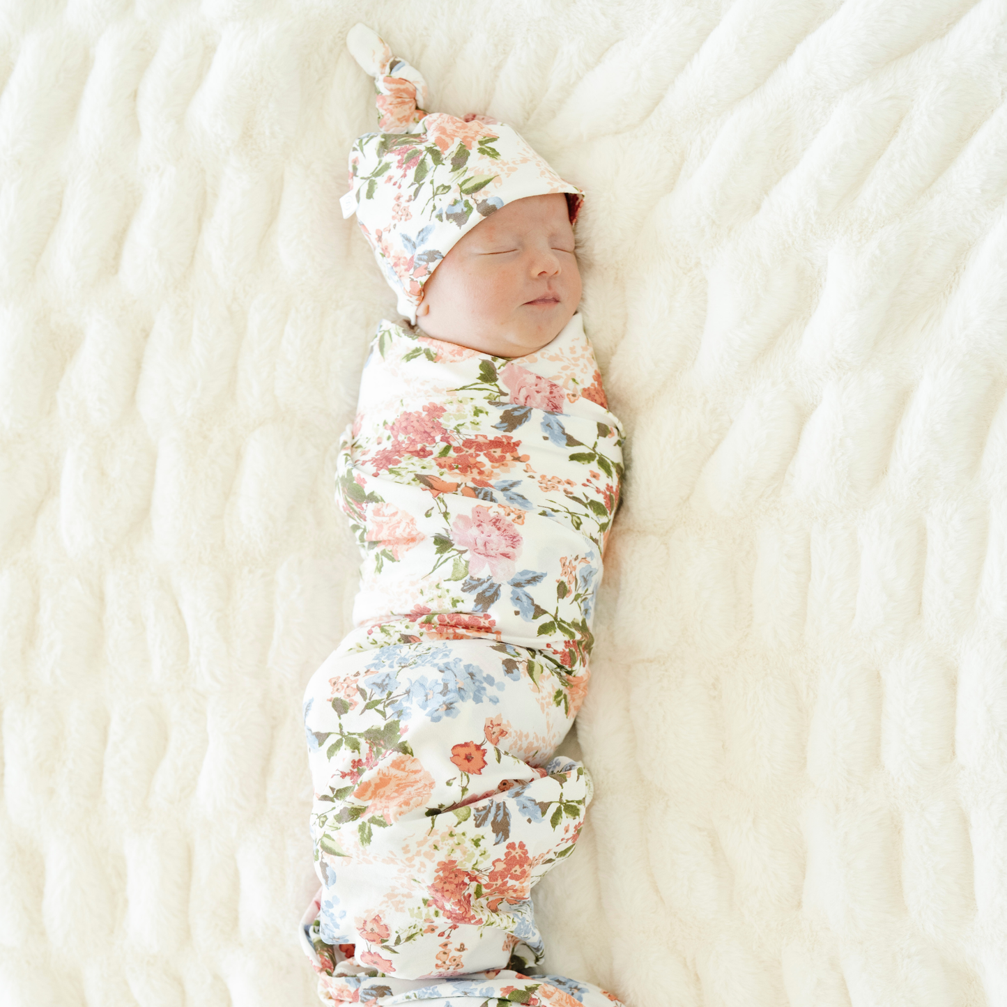 Baby girl swaddled in Vintage Floral Saranoni soft stretchy swaddle with a matching hat.