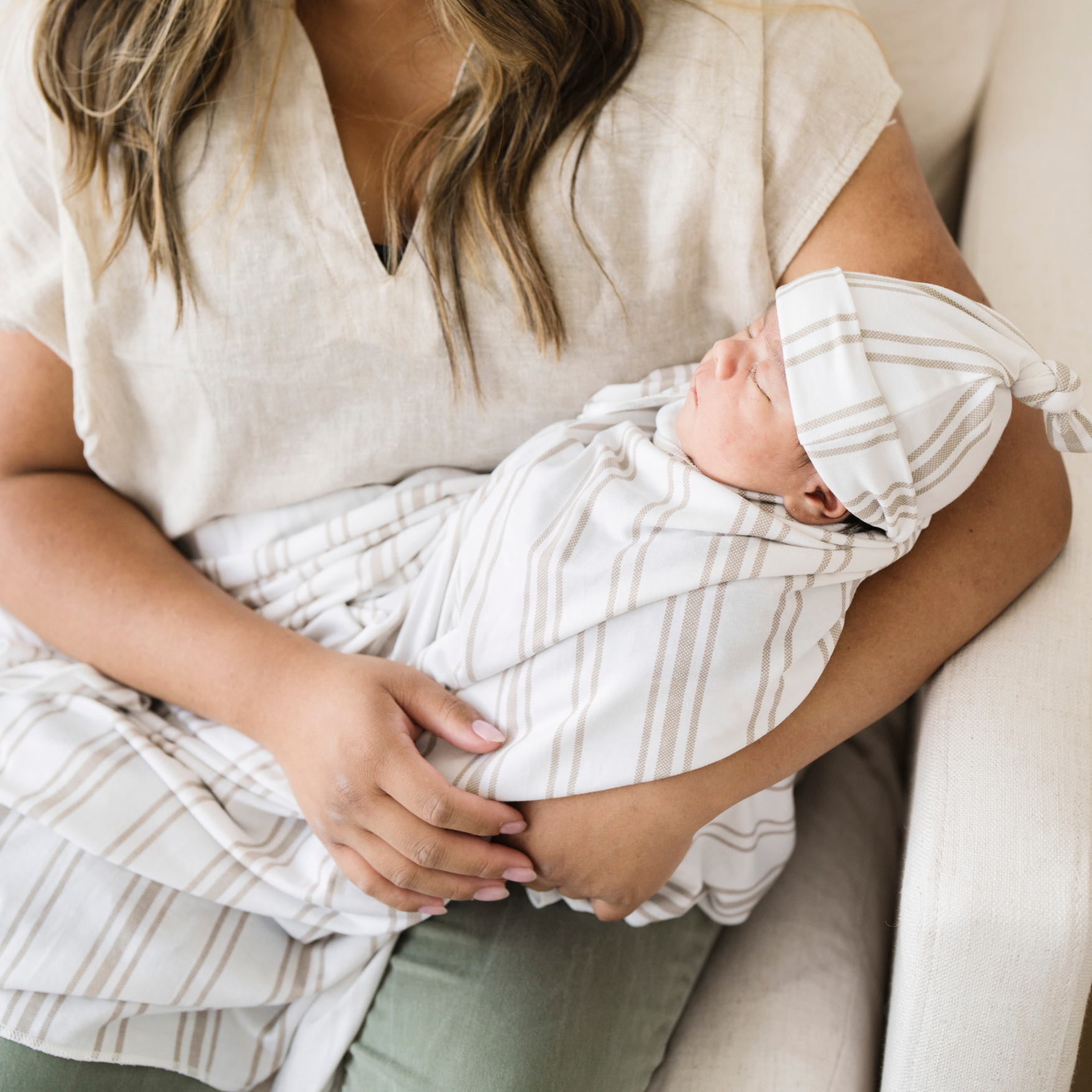 Mom holding baby boy swaddled in Saranoni soft stretchy swaddle in Taupe Stripe print with a matching hat. 