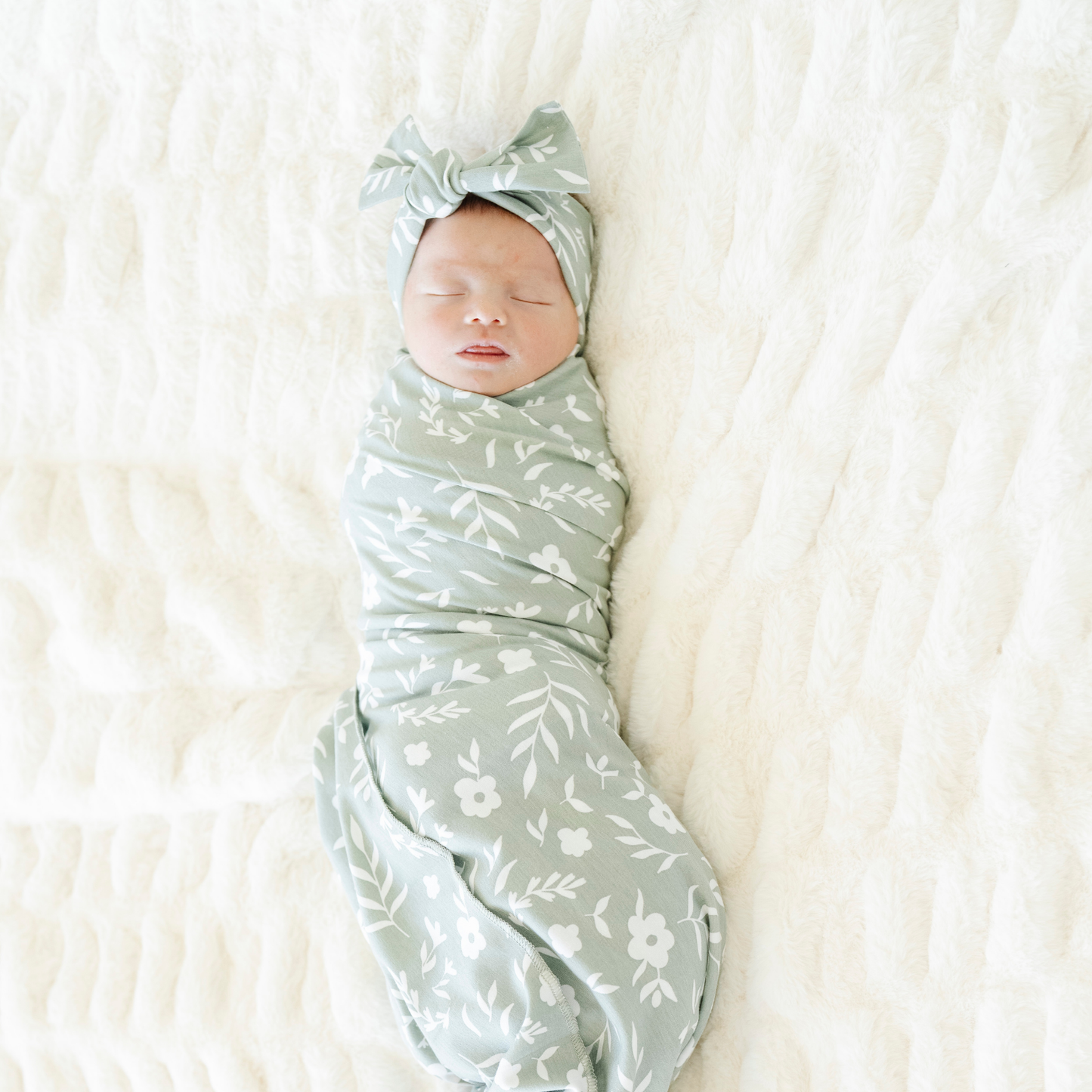 Baby girl swaddled in Saranoni Sweet Alyssum Stretchy Swaddle with a matching bow.