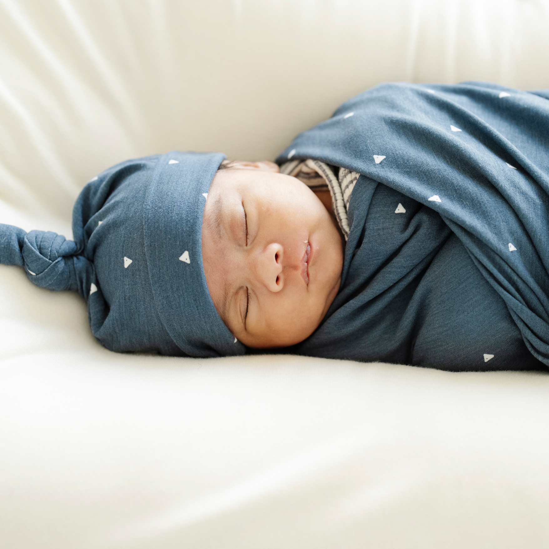 Baby boy swaddled in Denim Triangle Saranoni soft Stretchy Swaddle with a matching hat. 
