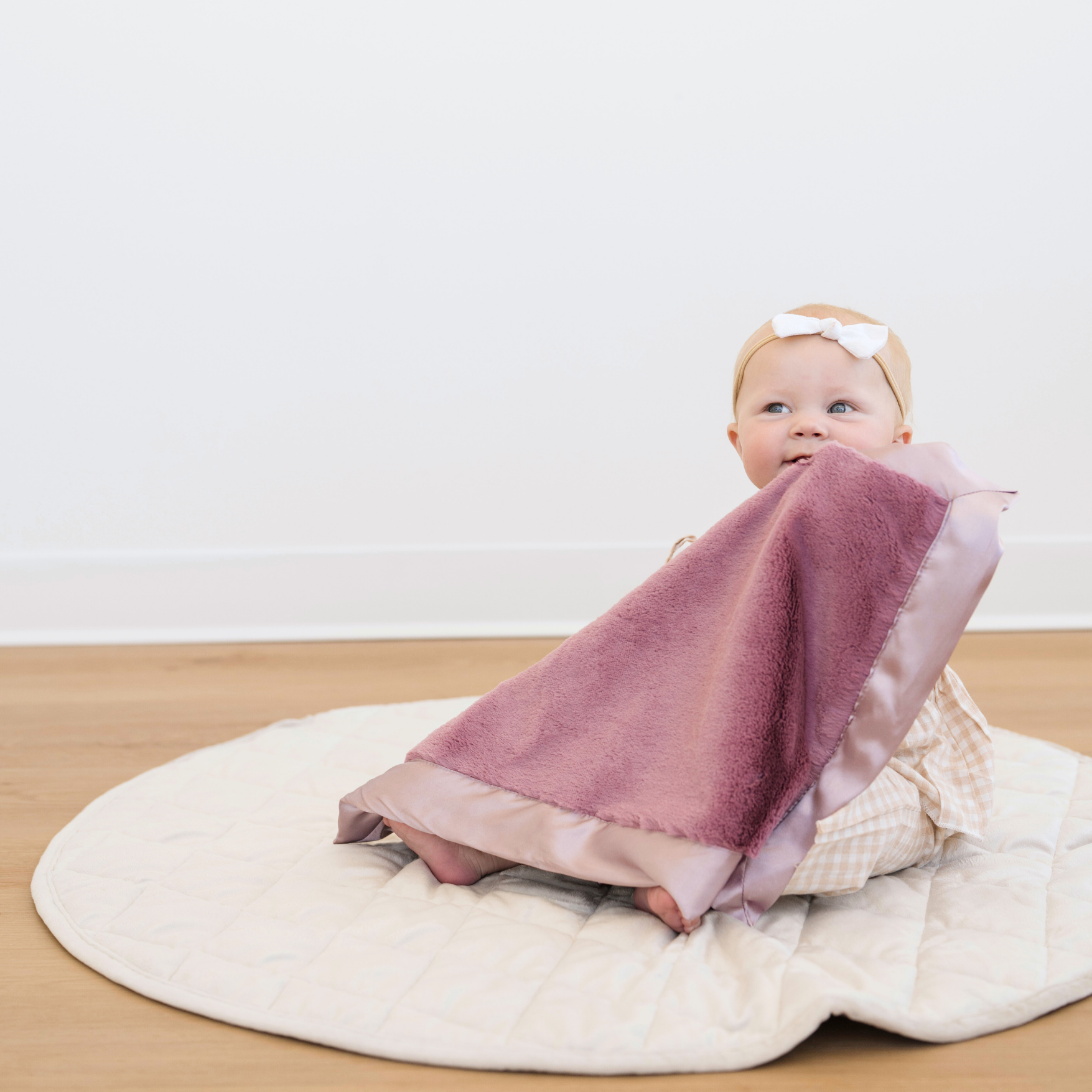 Baby girl holding Satin Border Mini baby blanket in Muted Mauve. 