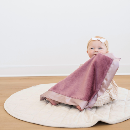Baby girl holding Satin Border Mini baby blanket in Muted Mauve. 
