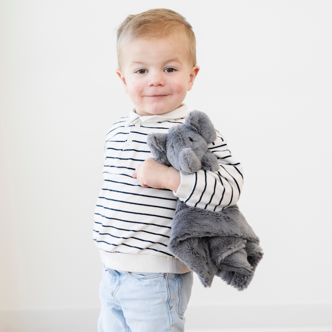 A little boy hugs a gray elephant stuffed animal lovey. This stuffed animal has a soft lush fabric and it's a great baby gift or toddler gift. Add this cute lovey to a nursery or bedroom to give your little one comfort just their size. 