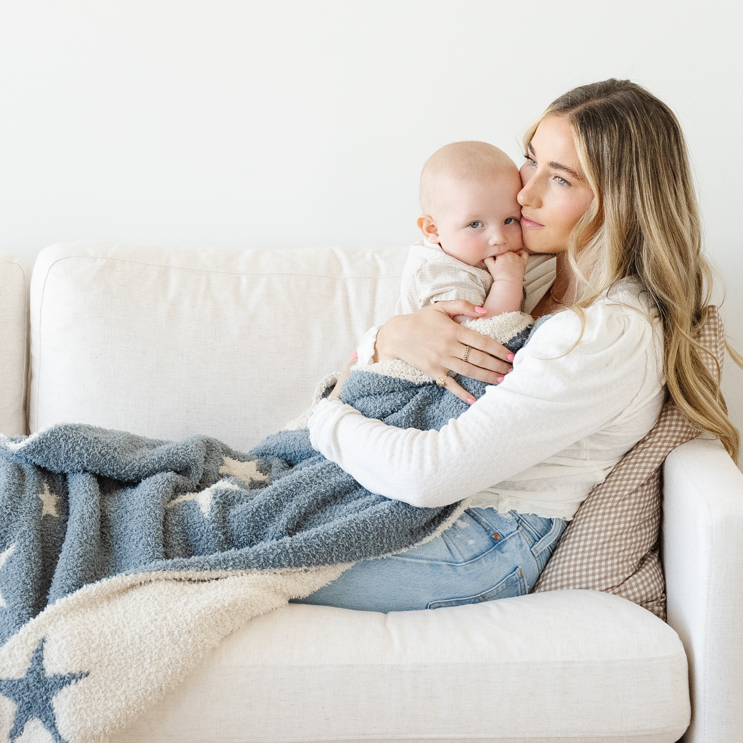 Mom snuggles little boy wrapped in a blue and tan blanket with stars on it. 