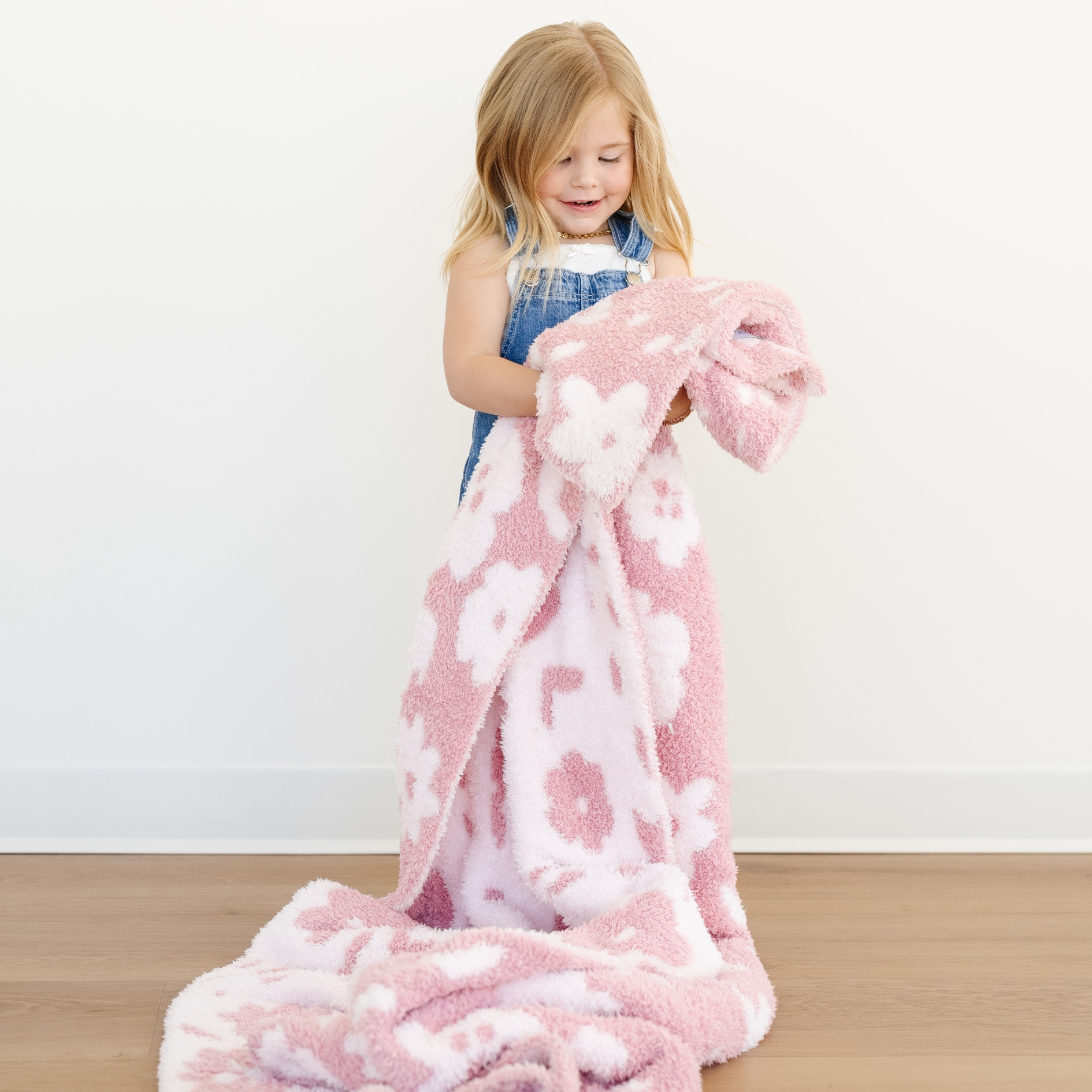 Little girl stands snuggled with a pink double layer bamboni toddler blanket. 