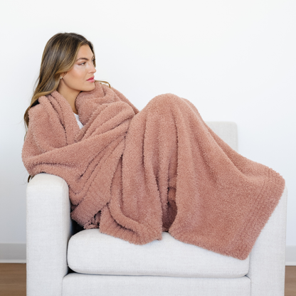 Woman sits on couch wrapped in a French Rose Bamboni XL blanket