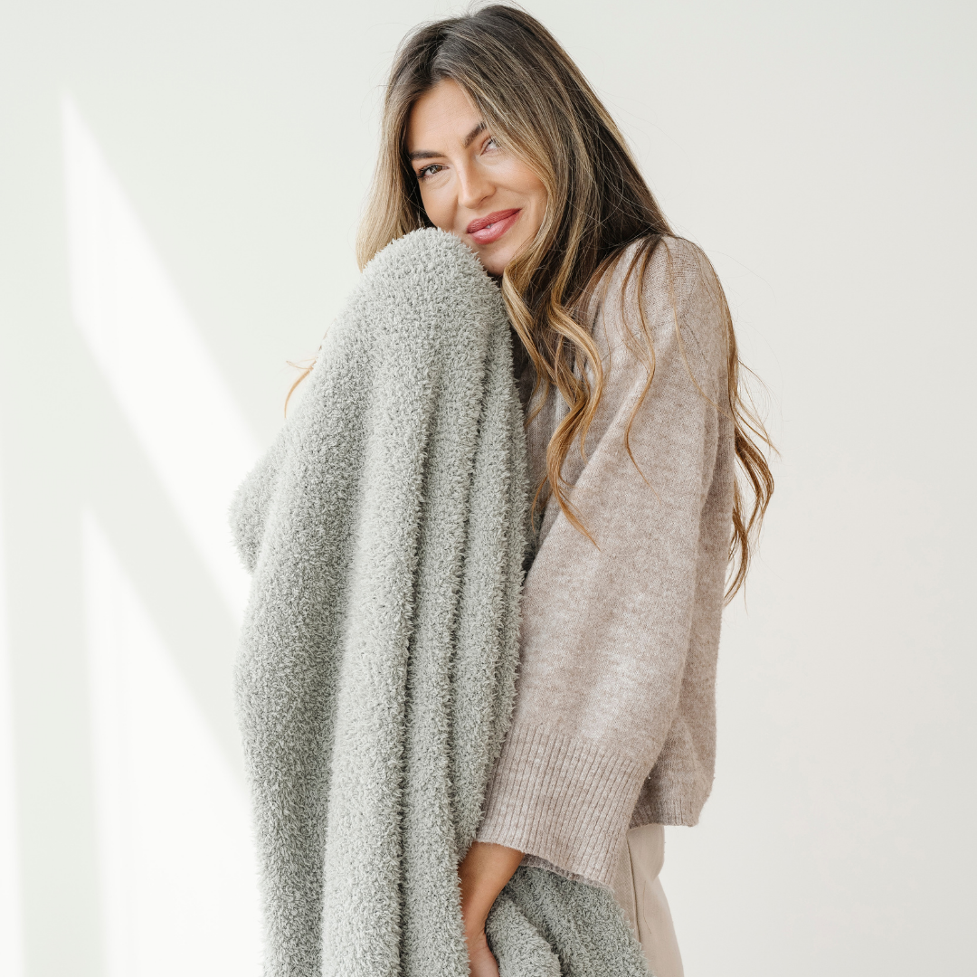 A woman holds a sage colored Bamboni® blanket that is an extra-large blanket. Perfect for relaxing, gifting, or as a home decor staple, this luxury blanket is a Saranoni blanket. This blanket is super breathable, stretchy, and soft. 