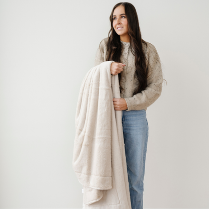 A woman smiles and holds a cream blanket that is a lush blanket. This soft blanket is a luxury blanket and a Saranoni blanket. Perfect as a home decor staple, for gifting, or for relaxation, this extra large throw blanket is sure to elevate and bring everyday luxury to your home. Enjoy this cozy blanket for years to come. 