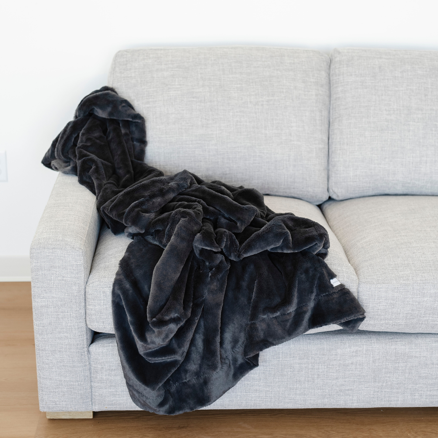 A charcoal lush Saranoni blanket is beautifully draped on a couch. This luxury blanket is a cozy blanket and a faux fur blanket. This soft blanket is great as a home decor staple, comfort gift, or everyday comfort item. Elevate your home and home decor with this luxury blanket that is also a throw blanket. Enjoy this cozy blanket for years to come.