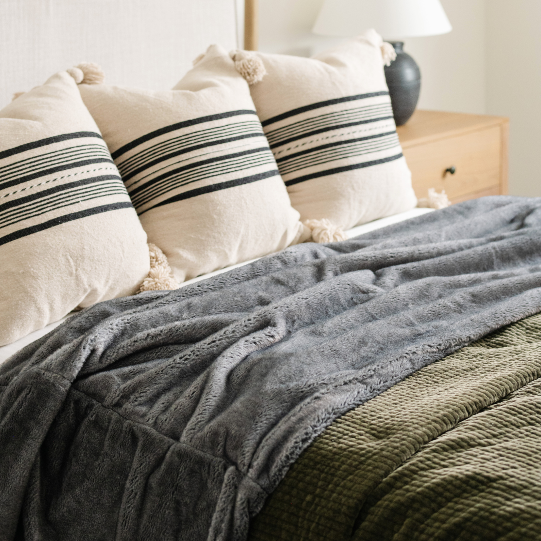 On a bed is a Saranoni Grand Faux Fur blanket, featuring an elegant light charcoal tone and luxuriously soft texture. This cozy, queen-sized blanket and faux fur blanket offers soothing weight, premium softness, timeless comfort, and is a soft blanket. Perfect as a big blanket and luxury blanket for snuggling or as a luxury bedroom accent, this Saranoni blanket elevates every cozy moment and is a cozy blanket.