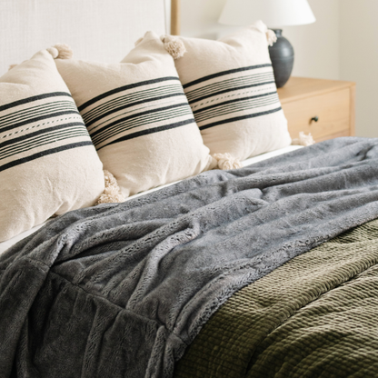 On a bed is a Saranoni Grand Faux Fur blanket, featuring an elegant light charcoal tone and luxuriously soft texture. This cozy, queen-sized blanket and faux fur blanket offers soothing weight, premium softness, timeless comfort, and is a soft blanket. Perfect as a big blanket and luxury blanket for snuggling or as a luxury bedroom accent, this Saranoni blanket elevates every cozy moment and is a cozy blanket.