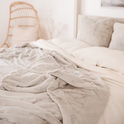 Draped on a bed is a Saranoni Grand Faux Fur blanket, featuring an elegant light cream/gray tone and luxuriously soft texture. This cozy, queen-sized blanket and faux fur blanket offers soothing weight, premium softness, timeless comfort, and is a soft blanket. Perfect as a big blanket and luxury blanket for snuggling or as a luxury bedroom accent, this Saranoni blanket elevates every cozy moment and is a cozy blanket.