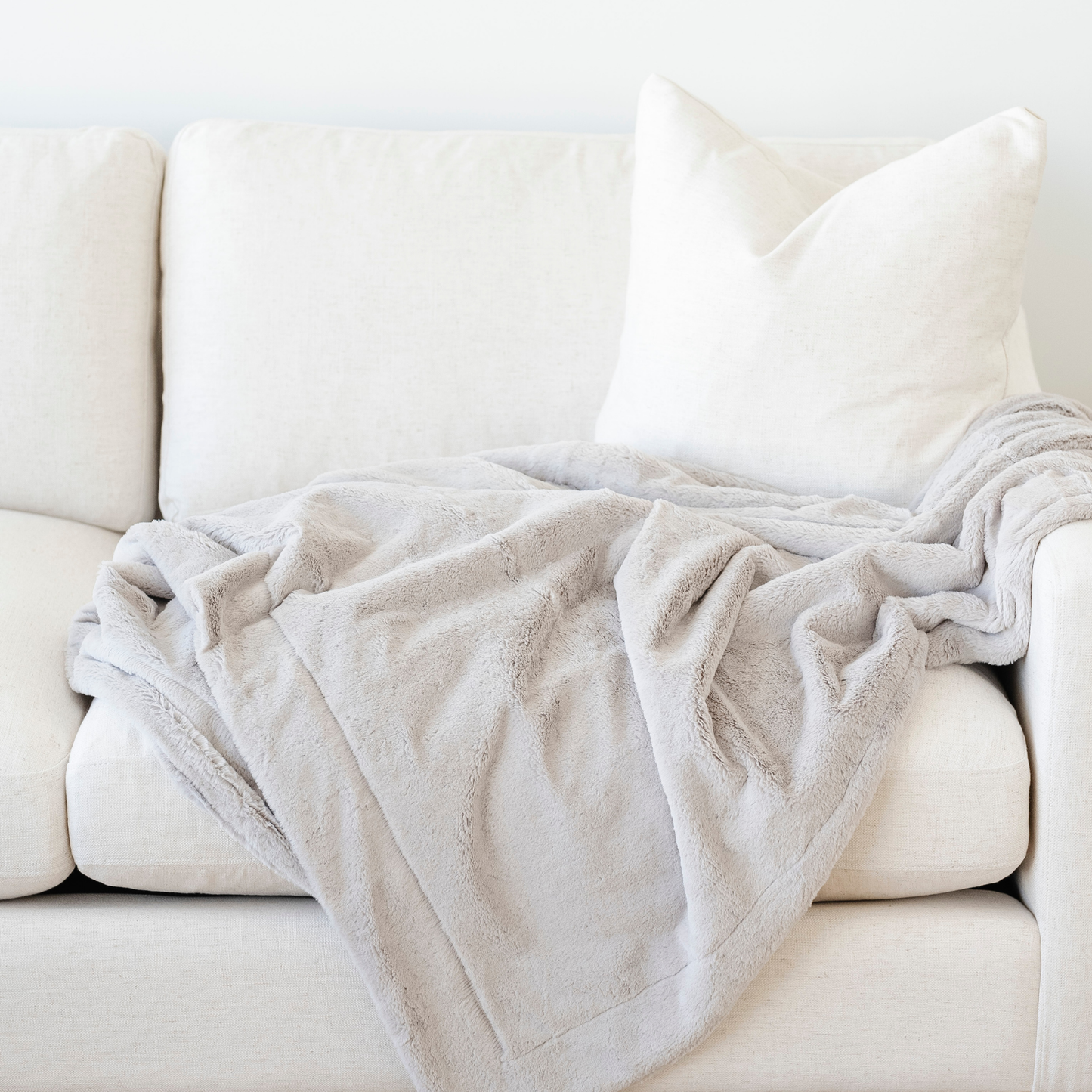 A gorgeous light gray blanket is draped on a cream couch. This soft blanket is a lush blanket and a Saranoni blanket. This luxury blanket is such a cozy blanket and is great for relaxing, gifting, or as a home decor staple. Enjoy this extra large blanket for years to come. 