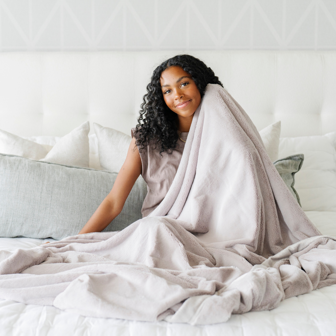 A woman holds a Feather (light gray) Lush XL Saranoni blanket, designed for oversized comfort and featuring a buttery soft, plush texture. This luxurious Saranoni blanket is perfect for cozy evenings, reading, or home decor. The Saranoni blanket adds warmth, style, and unmatched softness, making it an ideal gift or essential for ultimate relaxation.