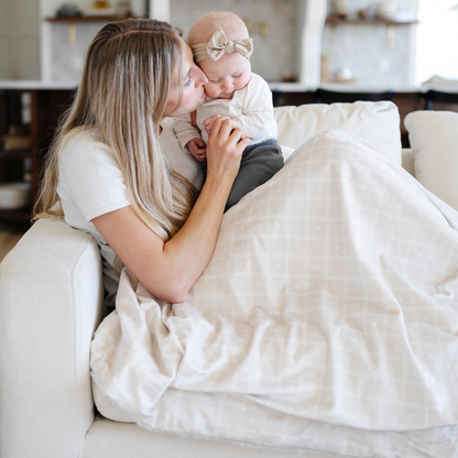 A mother holds her little girl and is sitting with a luxuriously soft Saranoni minky/lush blanket. This premium dual-textured throw features Saranoni’s signature cream lush fabric on one side and ultra-soft square printed minky on the other. Designed for ultimate relaxation, this plush blanket is perfect for snuggling, movie nights, and adding a touch of luxury to any home. This soft blanket is a luxury blanket and a Saranoni blanket. The cozy blanket is a perfect comfort item and a comfortable blanket. 