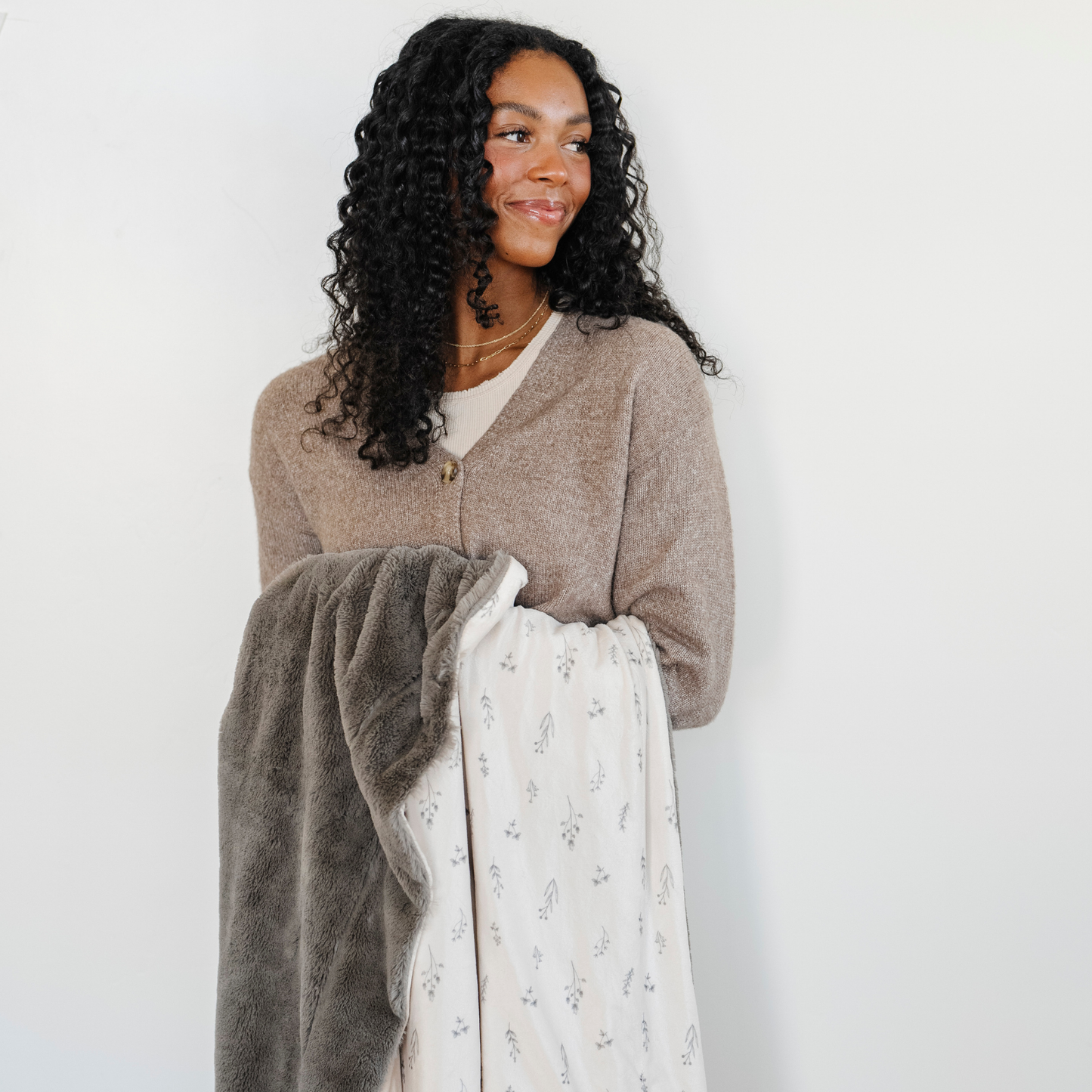 A woman holds a luxuriously soft Saranoni minky/lush blanket. This premium dual-textured throw blanket features Saranoni’s signature gray lush fabric on one side and ultra-soft floral printed minky on the other. This plush blanket is perfect for snuggling, movie nights, and adding a touch of luxury to any home. This soft blanket is a luxury blanket and a Saranoni blanket. The cozy blanket is a perfect comfort gift and is also beautiful for home decor. Enjoy this comfortable blanket!