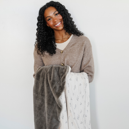 A woman smiles and holds a luxuriously soft Saranoni minky/lush blanket. This premium dual-textured throw blanket features Saranoni’s signature gray lush fabric on one side and ultra-soft floral printed minky on the other. This plush blanket is perfect for snuggling, movie nights, and adding a touch of luxury to any home. This soft blanket is a luxury blanket and a Saranoni blanket. The cozy blanket is a perfect comfort gift and is also beautiful for home decor. Enjoy this comfortable blanket!