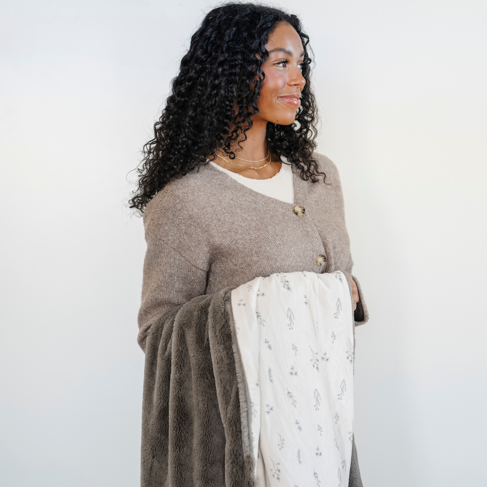 A woman holds a luxuriously soft Saranoni minky/lush blanket. This premium dual-textured extra-large throw blanket features Saranoni’s signature gray lush fabric on one side and ultra-soft floral printed minky on the other. This plush blanket is perfect for snuggling, movie nights, and adding a touch of luxury to any home. This soft blanket is a luxury blanket and a Saranoni blanket. The cozy blanket is a perfect comfort gift and is also beautiful for home decor. Enjoy this comfortable blanket!