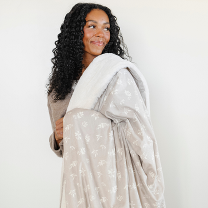 A woman smiles and holds a soft Saranoni minky/lush blanket. This throw blanket features Saranoni’s signature cream lush fabric on one side and ultra-soft floral printed minky on the other. Designed for ultimate relaxation, this high-quality, plush blanket is perfect for snuggling, movie nights, and adding a touch of luxury to any home. This soft blanket is a luxury blanket and a Saranoni blanket. The cozy blanket is a perfect comfort gift and is also beautiful for home decor and relaxation. 