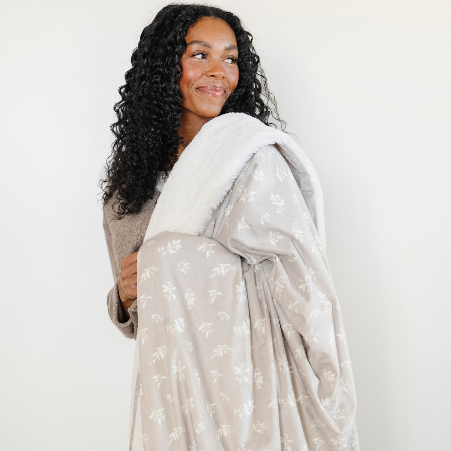 A woman smiles and holds a soft Saranoni minky/lush blanket. This extra large throw blanket features Saranoni’s signature cream lush fabric on one side and ultra-soft floral printed minky on the other. Designed for ultimate relaxation, this high-quality, plush blanket is perfect for snuggling, movie nights, and adding a touch of luxury to any home. This soft blanket is a luxury blanket and a Saranoni blanket. The cozy blanket is a perfect comfort gift and is also beautiful for home decor and relaxation. 