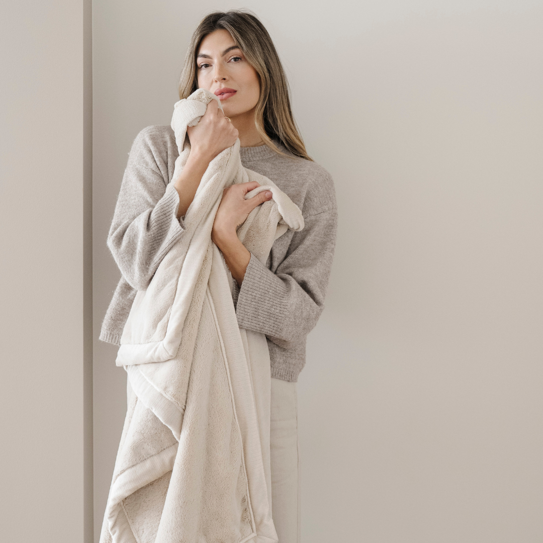 A woman holds a light cream blanket that is a lush blanket. This Saranoni blanket is a super soft blanket and is also a luxury blanket. Use this extra large blanket for gifting, relaxing, or as a home decor staple. 
