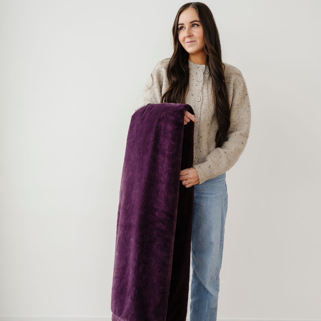A woman holds a dark purple lush blanket. This luxury blanket is a soft blanket and a Saranoni blanket. This extra large throw blanket is great for gifting, relaxing, or using for home decor. Enjoy this cozy blanket for years to come!