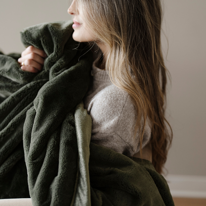 A woman holds a buttery-soft lush green blanket. This luxury blanket is a Saranoni blanket and is also an extra large throw blanket. This blanket is a great comfort gift, home decor staple, or for relaxing!