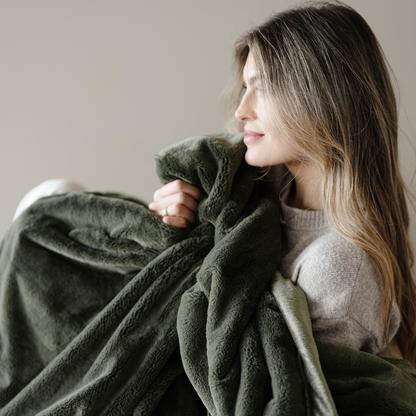 A woman is holding a green lush blanket. This luxury blanket is a cozy blanket and a Saranoni blanket. This soft blanket is great for gifting, relaxing, or as a home decor staple. Enjoy this extra large blanket for years to come. 