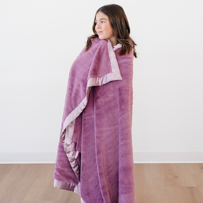 An adorable little girl is wrapped in a light purple blanket that is a toddler blanket and a lush blanket. This soft blanket has a cute satin border as well. This luxury blanket is a Saranoni blanket and is a great toddler gift or little girl gift. 