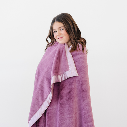 A little girl is wrapped in a light purple blanket that has a light purple satin border. This lush blanket is a soft blanket and a luxury blanket as well as a Saranoni blanket. This blanket is a great toddler gift or little girl gift. Embrace luxury that lasts with this toddler blanket. 