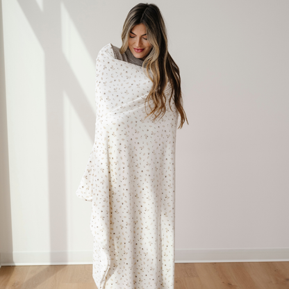 A woman is wrapped in a floral patterned minky stretch blanket. This extra large throw blanket is a Saranoni blanket that is perfect for gifting, lounging, and taking on the go. Enjoy this stretchy, durable, luxury blanket for years to come!