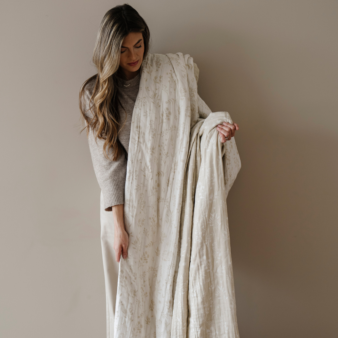 A woman holds a quilt that is a bamboo rayon muslin quilt. This soft blanket has a floral pattern and get softer with every wash. This luxury blanket is also a Saranoni blanket and it is a great gift, or relaxation blanket.