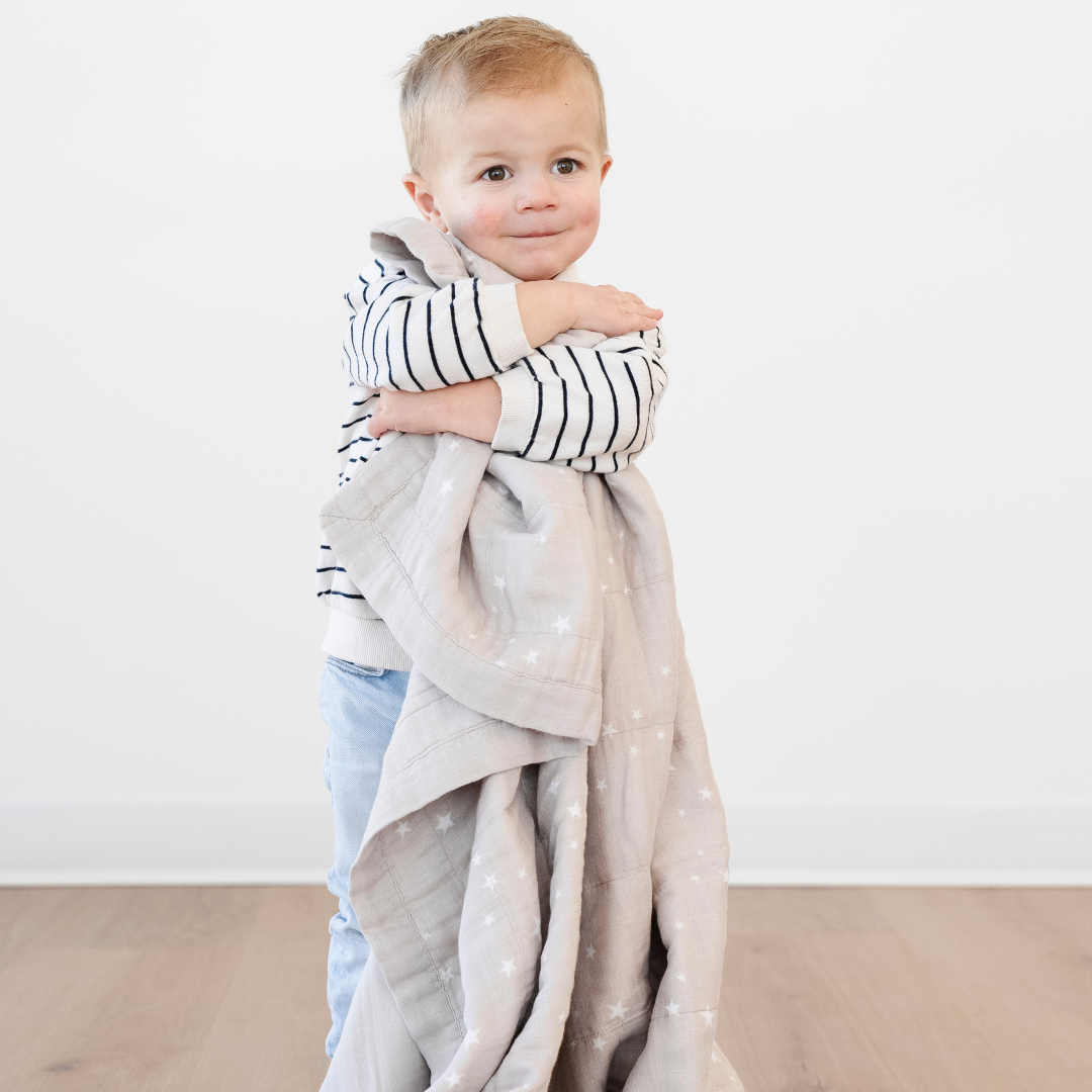 A little boy holds a bamboo rayon muslin quilt that has a little star pattern on it. This soft quilt is a Saranoni blanket and is a great toddler gift or baby gift. This muslin fabric gets softer with every wash, making it extra cozy. 