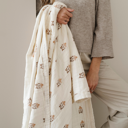 A woman holds a floral patterned bamboo rayon muslin quilt. This soft blanket get softer with every wash and is a Saranoni blanket. This blanket is a great comfort gift, relaxing blanket, or home decor staple. 