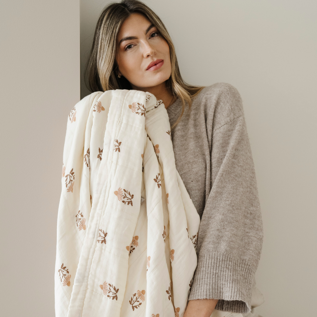 A woman is holding a bamboo rayon muslin quilt that is a floral pattern. This soft Saranoni blanket is a very luxurious blanket and is also great as a home decor item. Enjoy the muslin fabric that gets softer with every wash.