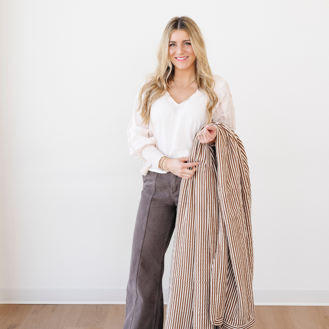 A smiling woman is holding a brown and white striped bamboo rayon muslin quilt. This soft blanket is a Saranoni blanket and is also very luxurious. This cozy blanket works great as a gift, relaxation blanket, or home decor staple. Enjoy this luxury blanket for years to come!