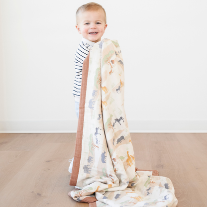 A smiling little boy is holding bamboo rayon muslin quilt that has a safari animal pattern on it. This soft blanket is a luxury blanket and a Saranoni blanket. The soft muslin fabric makes it a great baby gift, gift for toddlers, or addition to a bedroom or nursery. 