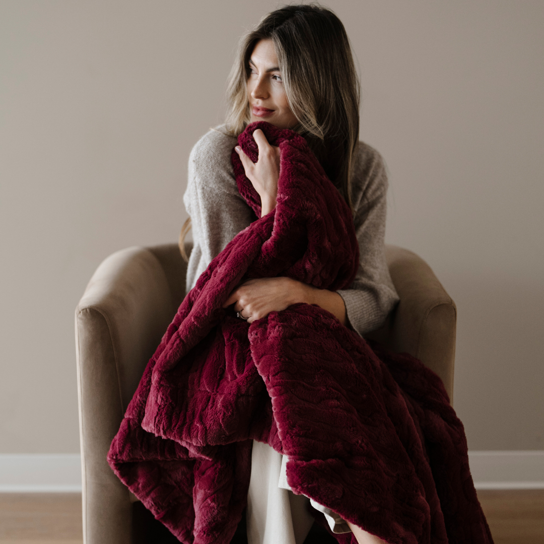 A woman holds a deep red patterned faux fur blanket. This luxury blanket is super cozy and is great for gifting, lounging, or home decor. Enjoy this Saranoni blanket for years to come. 