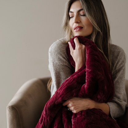 A woman is holding a deep red patterned faux fur blanket. This soft blanket is a Saranoni blanket and is great for luxury living. 