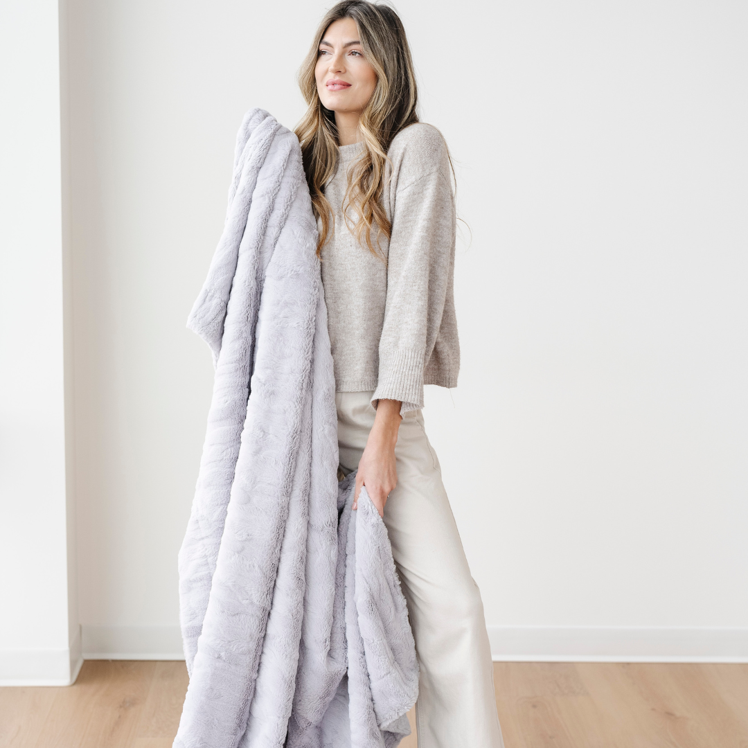 A woman is holding a light gray patterned faux fur blanket. This Saranoni blanket is luxuriously soft and works great as a comfort gift, relaxation item, or home decor staple. Enjoy this cozy blanket as it adds luxury to your home. 
