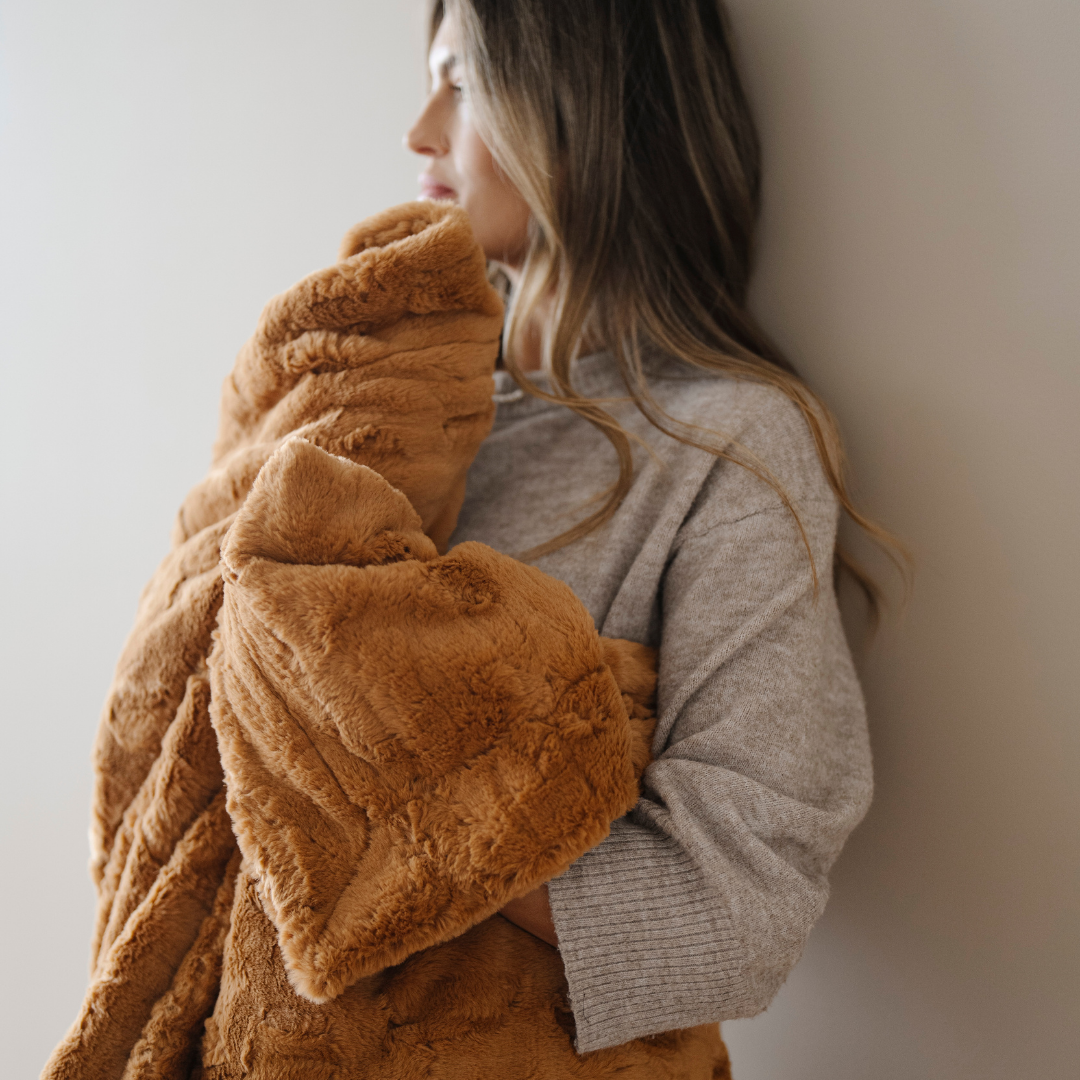 A woman is holding a copper colored patterned faux fur blanket. This Saranoni luxury blanket is a throw blanket and perfect for luxury living, gifting, and home decor. 