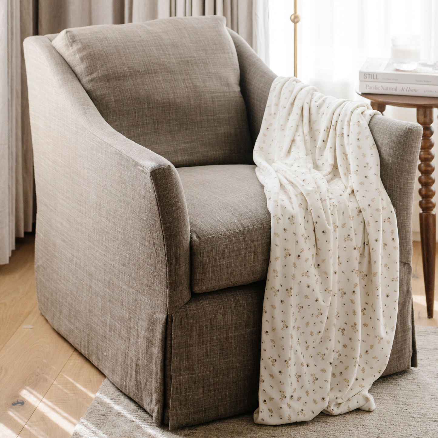 A floral patterned minky stretch blanket is draped on a chair. This soft blanket is a luxury blanket and Saranoni blanket. Use this stretchy, durable blanket for gifting, lounging, or on the go. 