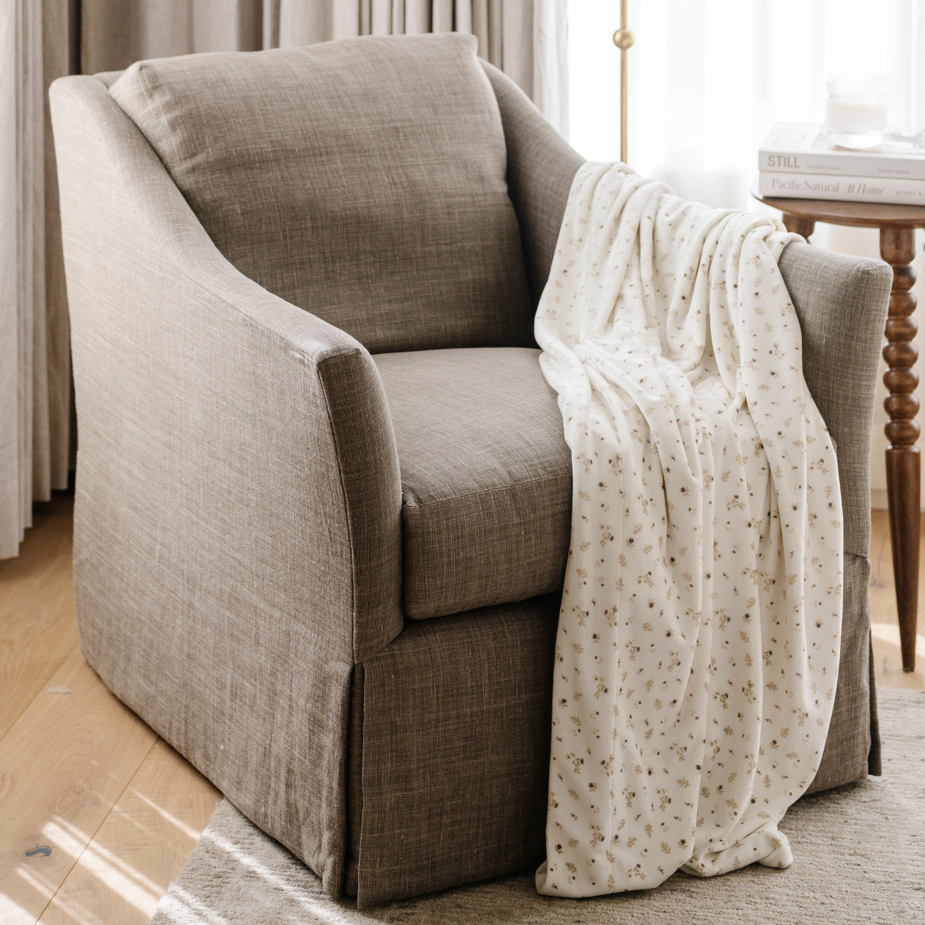 A floral patterned minky stretch blanket is draped on a chair. This soft blanket is a luxury blanket and Saranoni blanket. Use this stretchy, durable blanket for gifting, lounging, or on the go. 