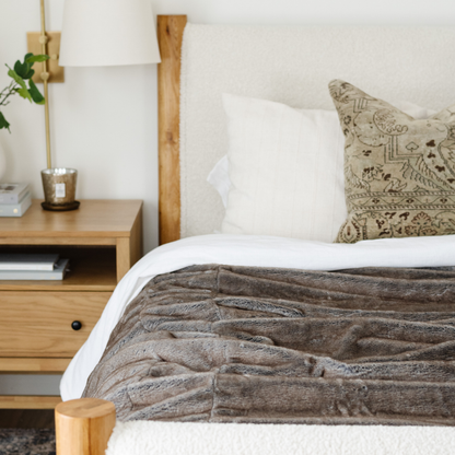 On a bed there is a Saranoni Grand Faux Fur blanket, featuring an elegant light brown tone and luxuriously soft texture. This cozy, queen-sized blanket and faux fur blanket offers soothing weight, premium softness, timeless comfort, and is a soft blanket. Perfect as a big blanket and luxury blanket for snuggling or as a luxury bedroom accent, this Saranoni blanket elevates every cozy moment and is a cozy blanket.