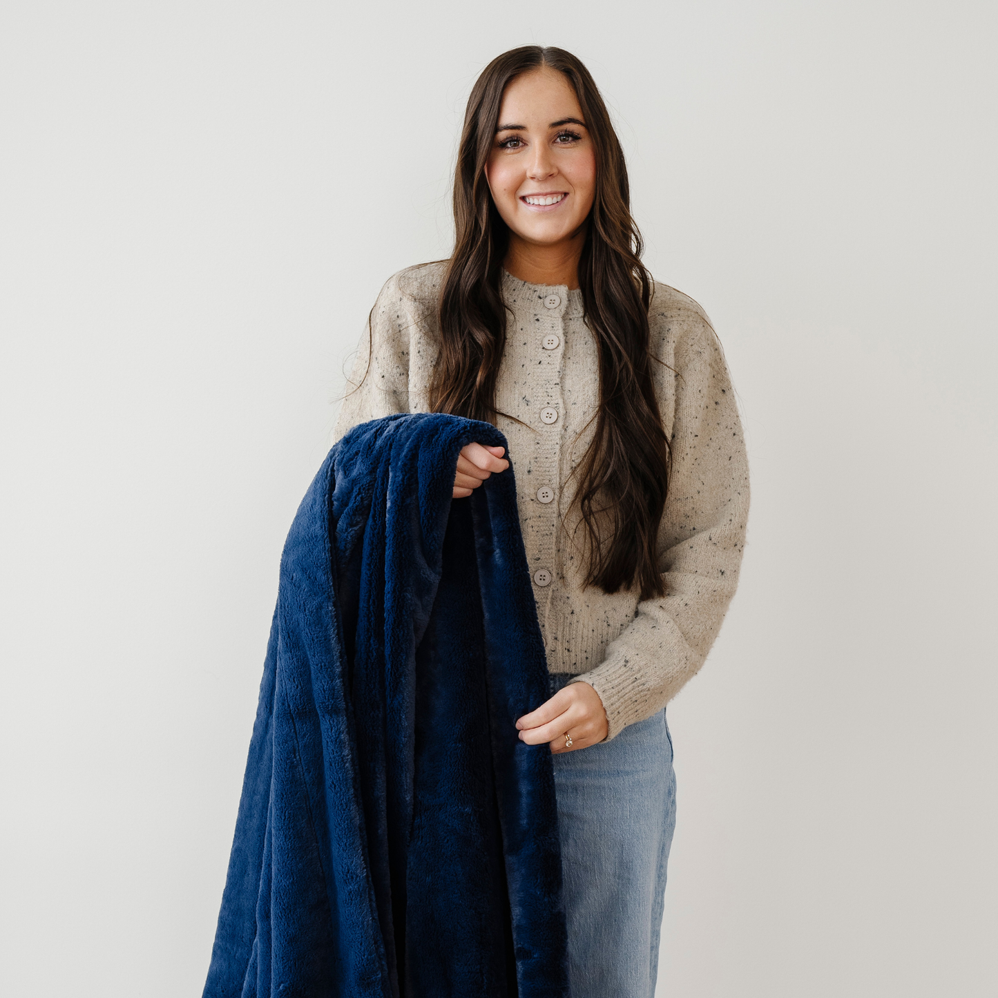 A woman smiles and holds a deep blue lush Saranoni blanket. This soft throw blanket is a cozy blanket and a faux fur blanket. This soft blanket is great as a home decor staple, comfort gift, or everyday relaxation item. Elevate your home and home decor with this faux fur blanket that is also a throw blanket. Enjoy this throw blanket for years to come.