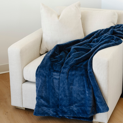 A deep blue lush Saranoni blanket is draped on a chair. This luxury blanket is a soft throw blanket and a faux fur blanket. This soft blanket is great as a home decor staple, comfort gift, or everyday relaxation item. Elevate your home and home decor with this faux fur blanket that is also a throw blanket. Enjoy this cozy blanket for years to come.